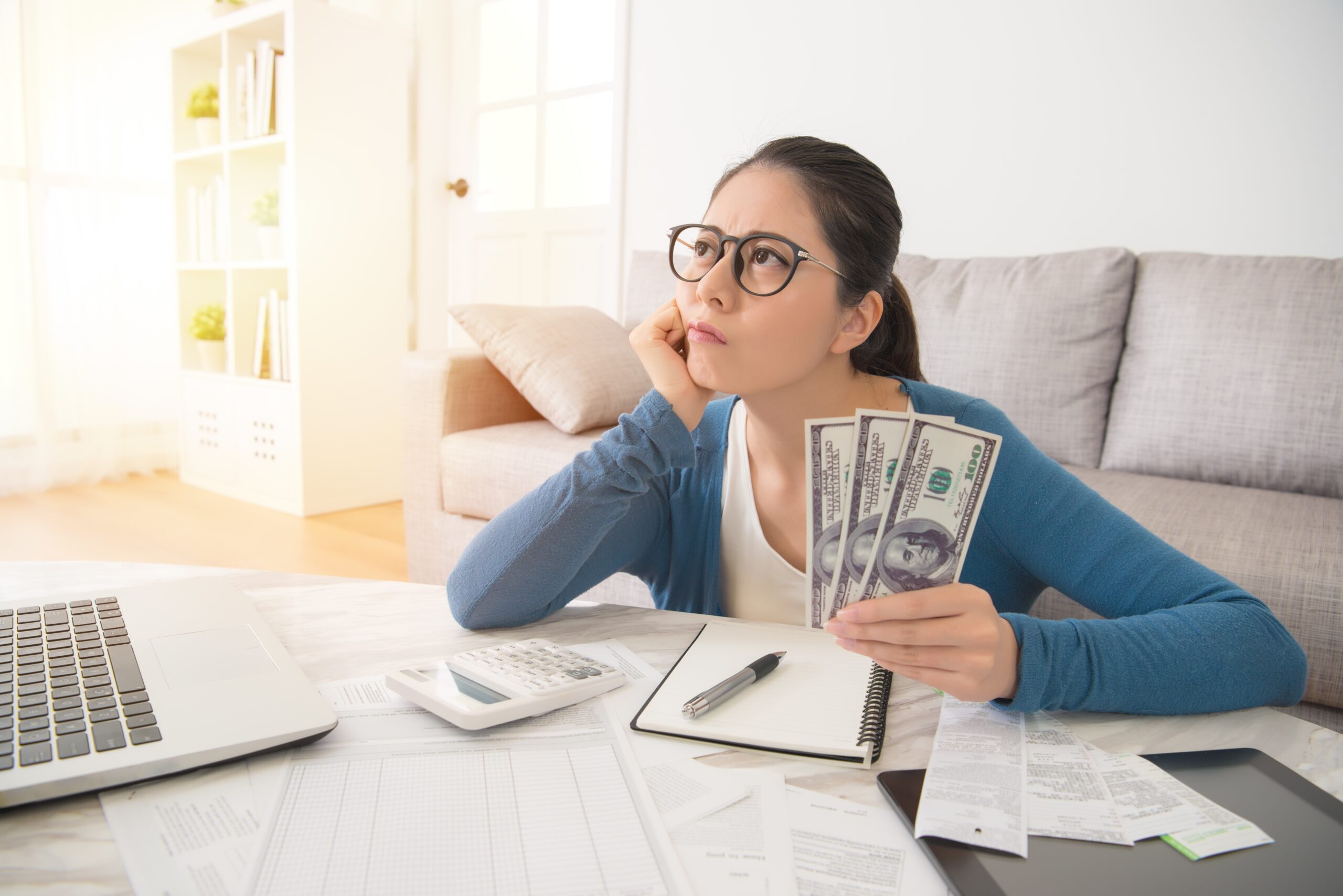 Attractive young mixed race asian woman working on finances worried about the expend cost sitting on sofa in the living room at home. interior and domestic housework concept.